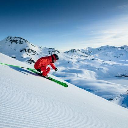 Skier in red suit carving down a groomed snowy slope in the Alps